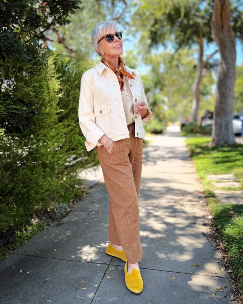 Susan B. wears a cropped chore jacket, polo henley tank, brown silk scarf, brown cotton pants, yellow velvet
