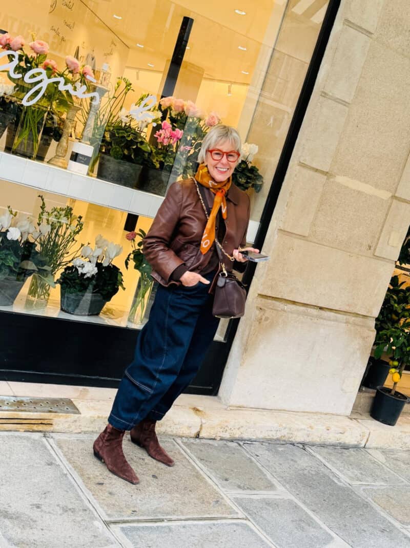 Susan B. wears dark wash barrel jeans and a brown leather jacket in Paris.