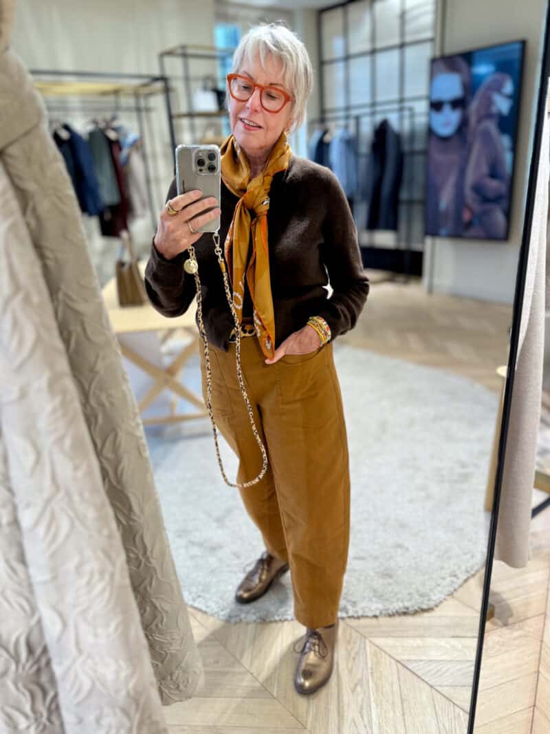 Susan B. takes a mirror selfie wearing a tan silk scarf, dark brown cardigan, tobacco brown pants, bronze derbies.