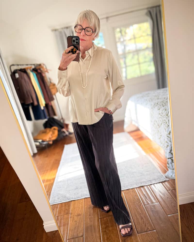 Susan B. wears an ivory silk shirt, brown pleated pants, long pearl necklace, kitten heel sandals.