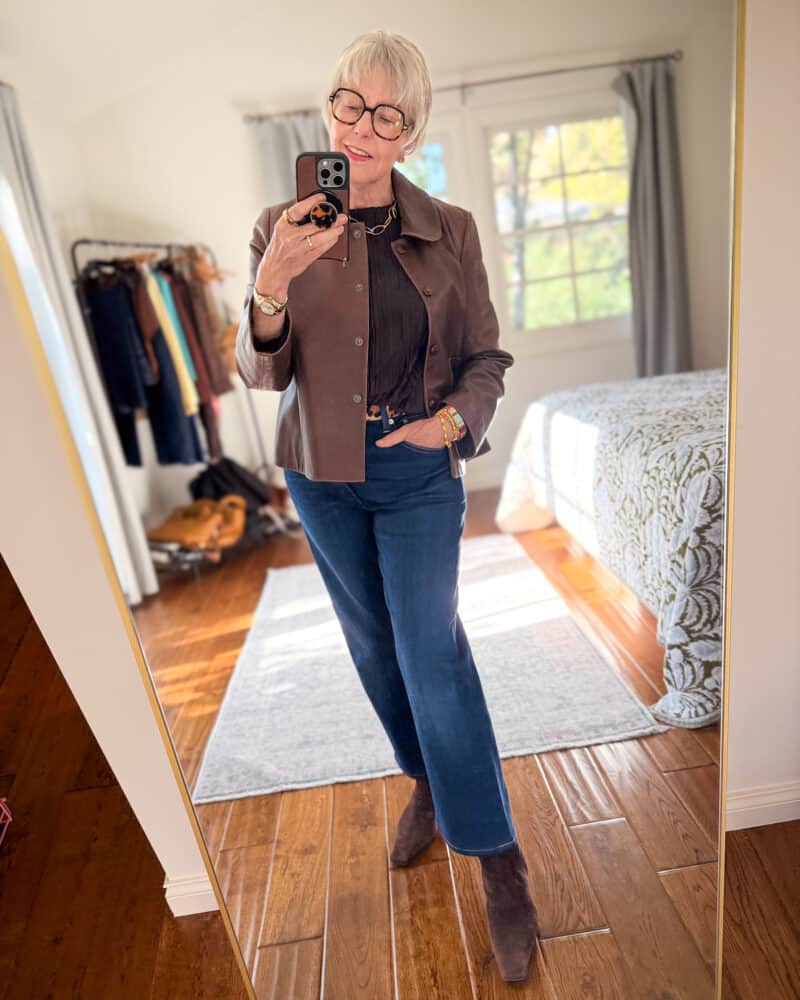 Susan B. wears a brown leather jacket, pleated brown top, leopard print belt, straight leg jeans, brown suede boots.