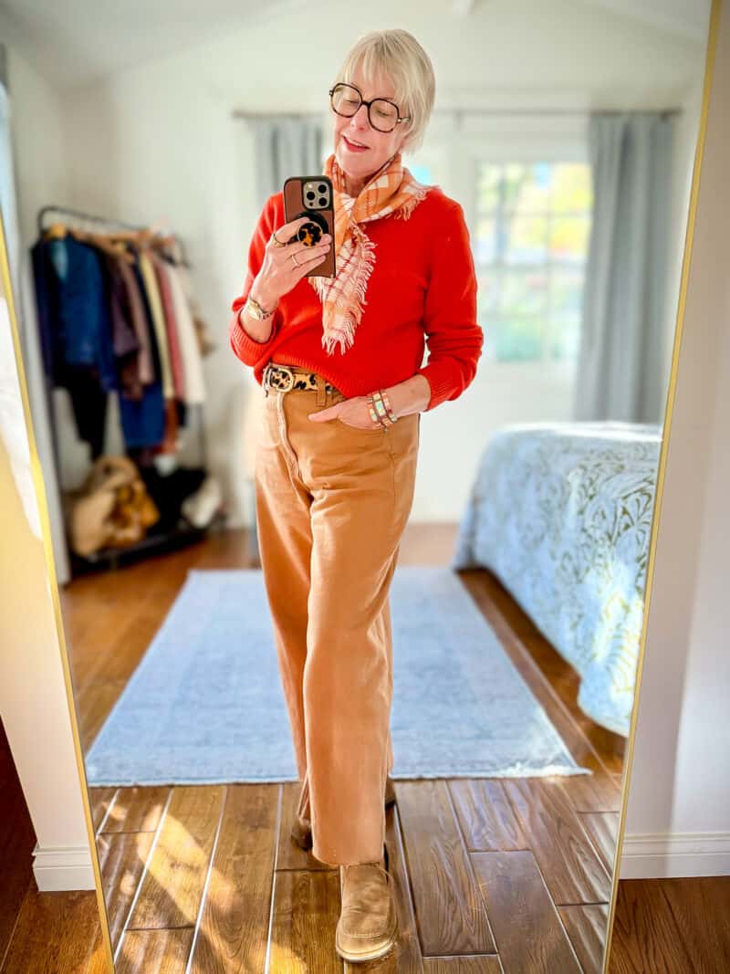 Susan B. wears a red sweater, cashmere bandana, leopard print belt, colored denim jeans, and suede loafers.