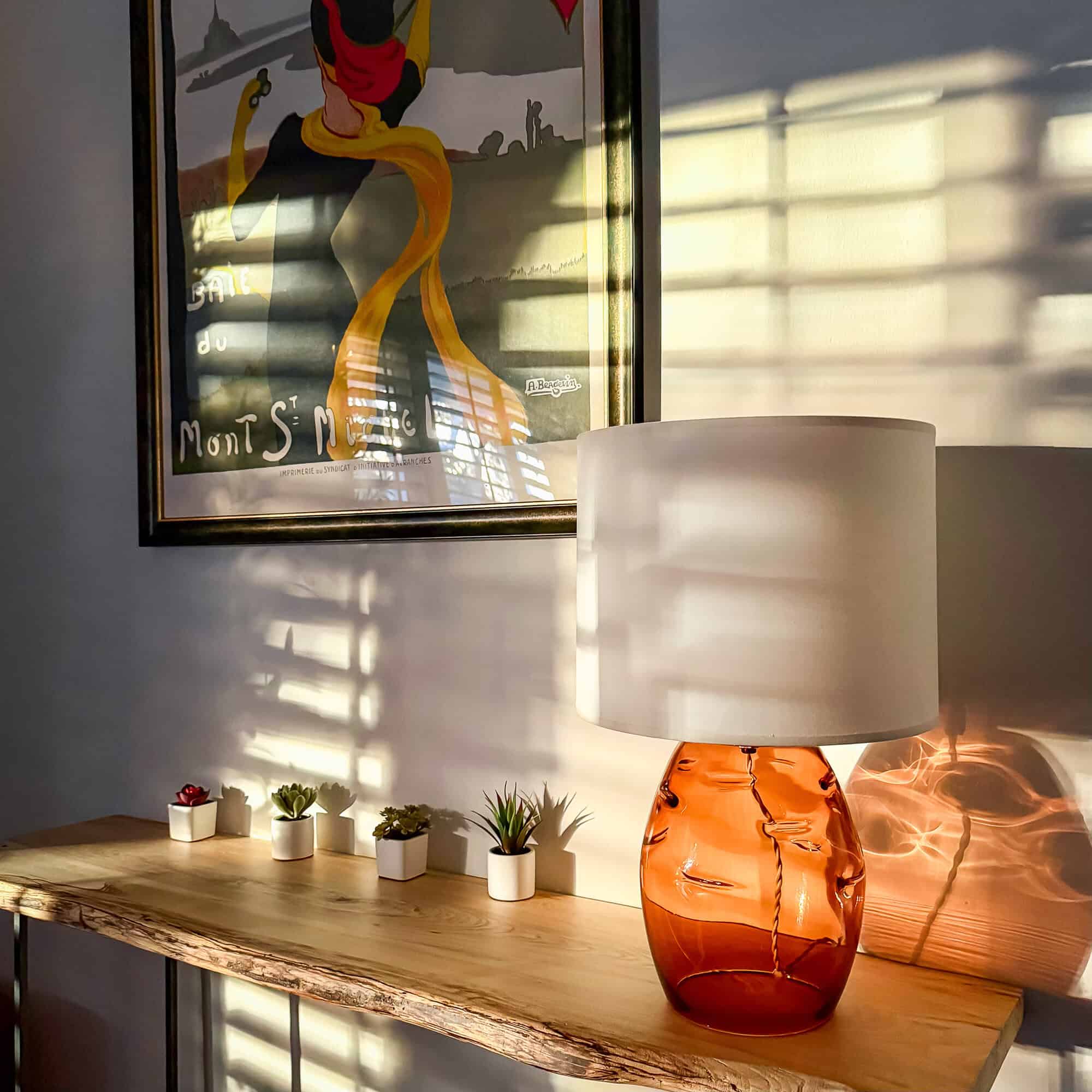 Sunlit entryway with a clean wood console, glass lamp, and wall art — a calm, decluttered space.