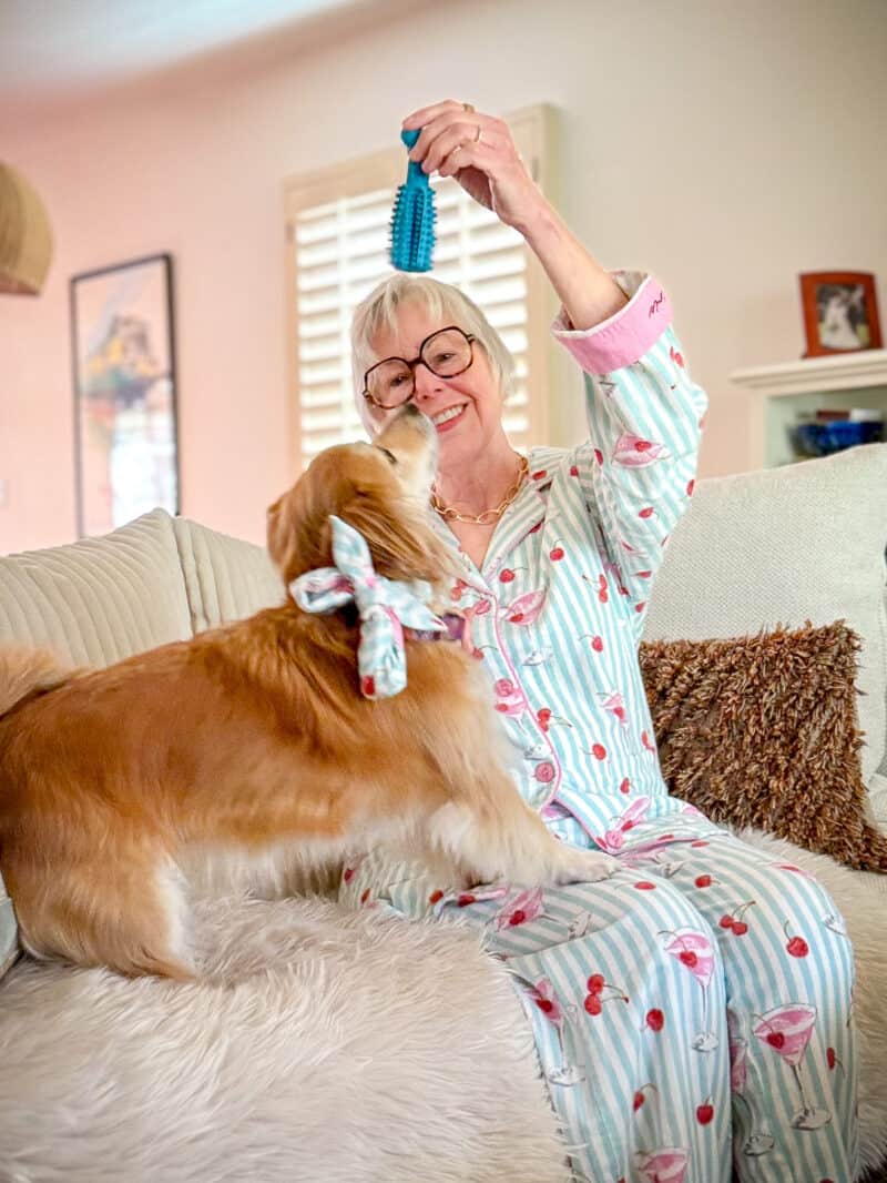 Susan B. wearing striped print flannel pajamas sits on a sofa holding a toy for her dog Bella.