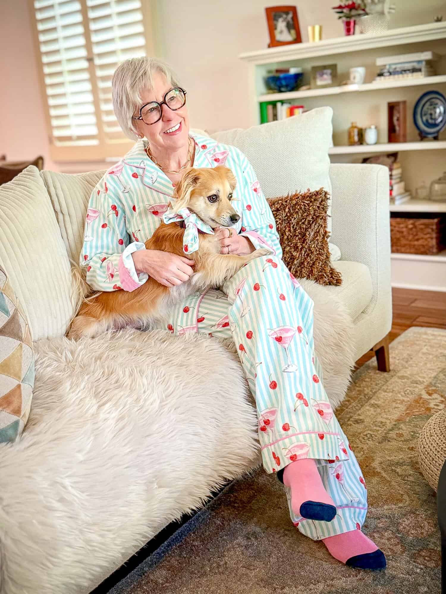 Susan B. wearing striped print flannel pajamas sits on a sofa with her dog Bella.