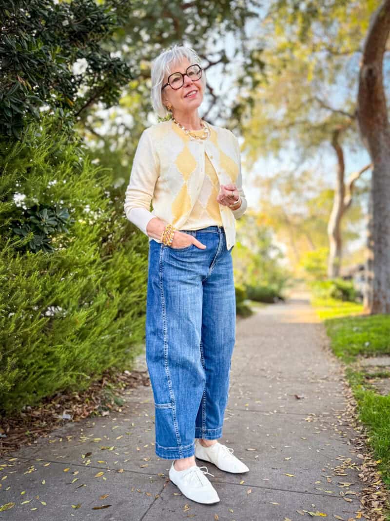 Denim trends for women over 50: barrel leg jeans styled with an argyle cardigan and off-white ballet oxfords.