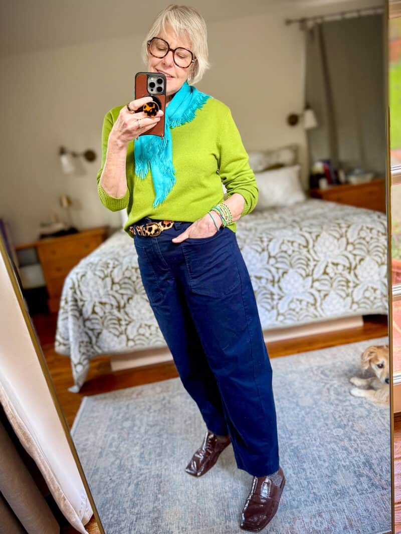 Susan B. wears an aqua fringed scarf, lime green sweater, Roxanne Assoulin beaded bracelets, leopard print belt, barrel leg navy trousers, brown patent square toe mules.