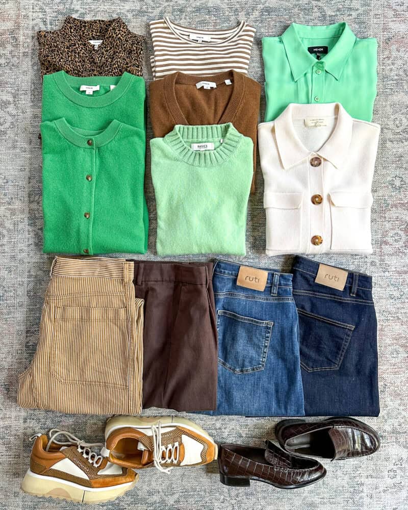 Flat lay of a 12-piece travel capsule wardrobe in brown, green, ivory, denim.
