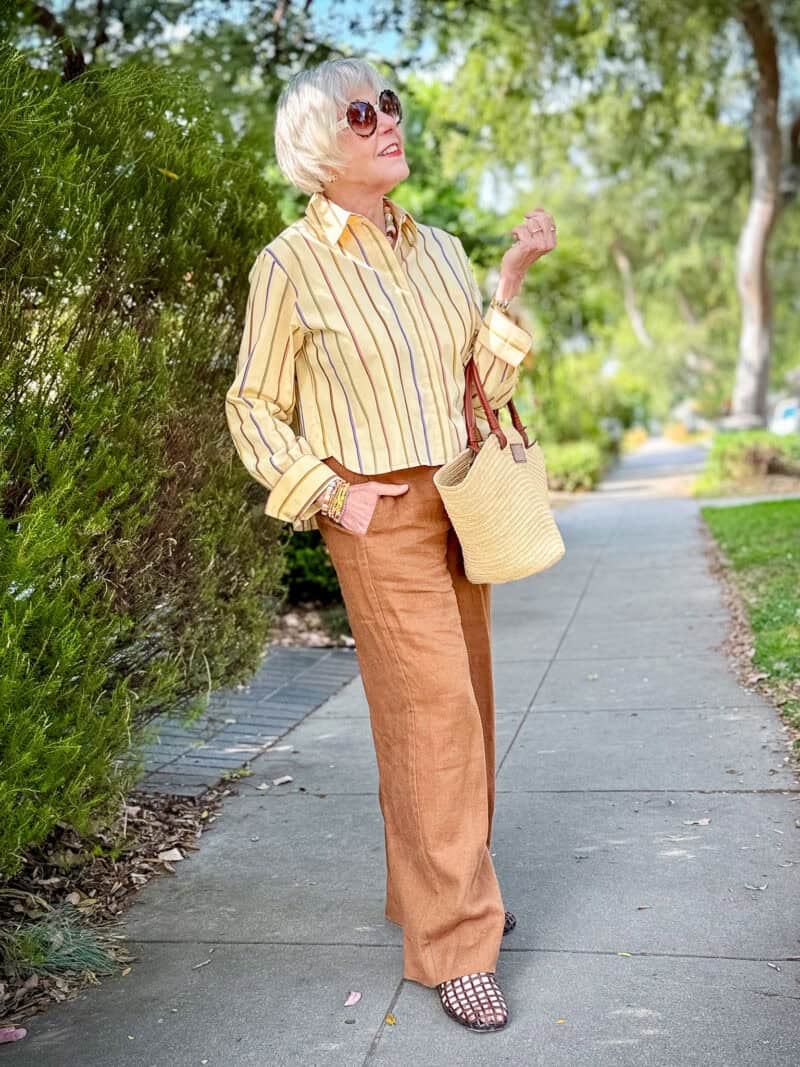 Susan B. wears a yellow striped cotton shirt with tan linen pants, jelly sandals, straw tote.