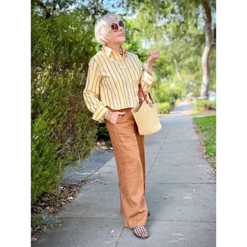 Susan B. wears a yellow striped cotton shirt with tan linen pants, jelly sandals, straw tote.
