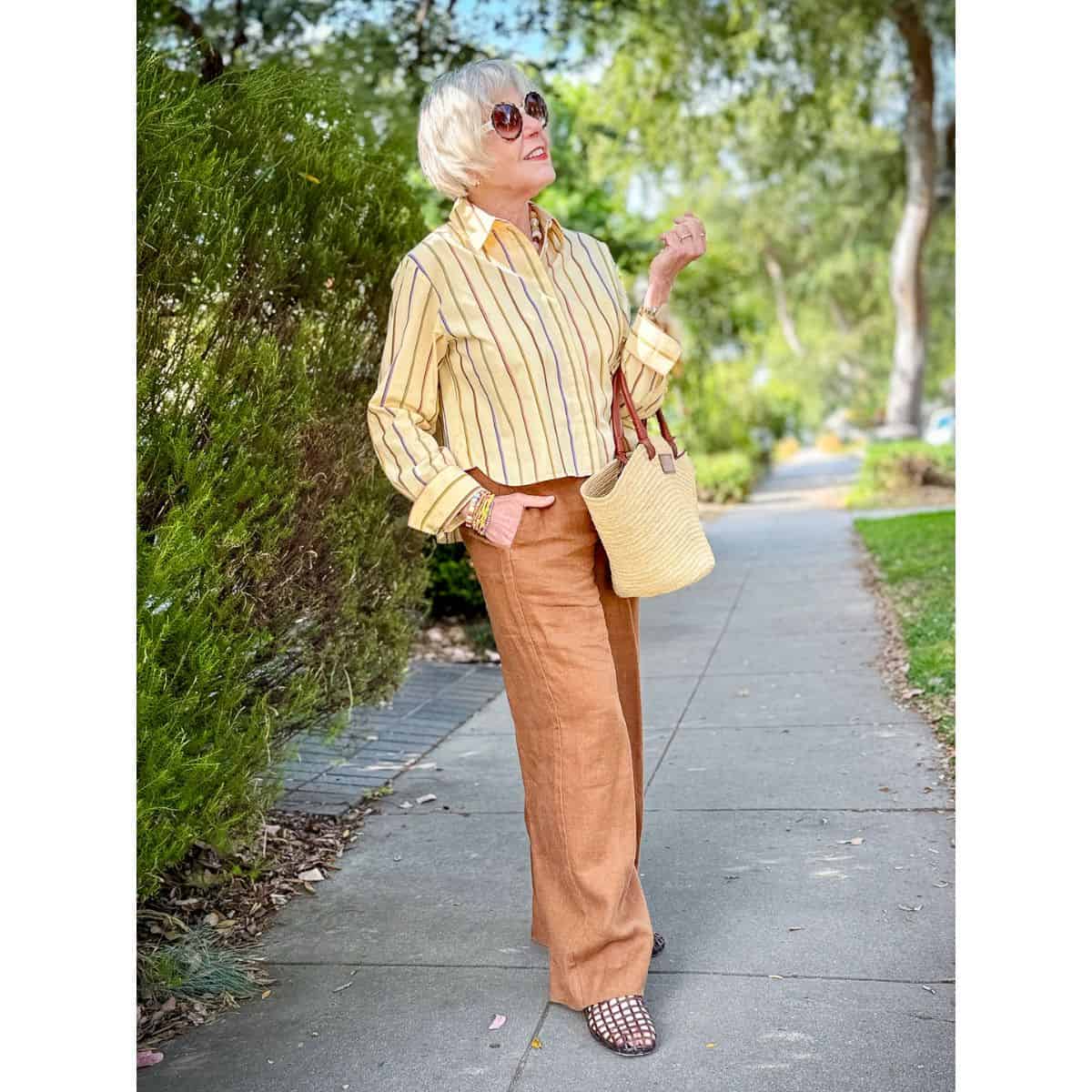 Susan B. wears a yellow striped cotton shirt with tan linen pants, jelly sandals, straw tote.