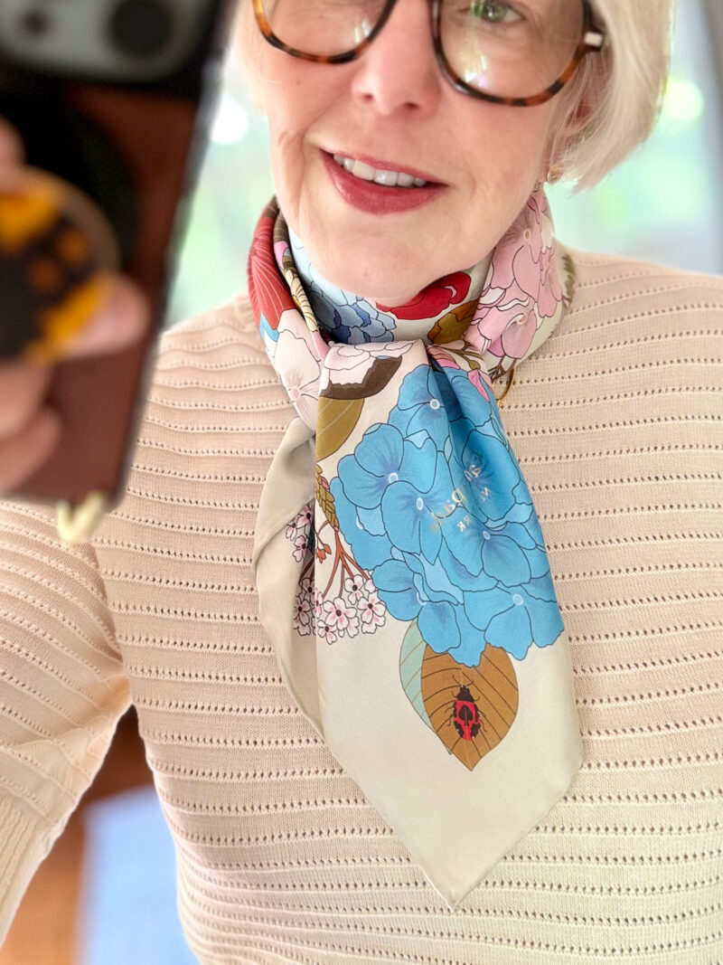 Mirror selfie with a floral print silk scarf tied Ascot-style, and textured ivory top.
