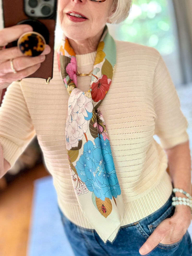 Mirror selfie with a floral print silk scarf, short sleeve sweater, blue jeans.