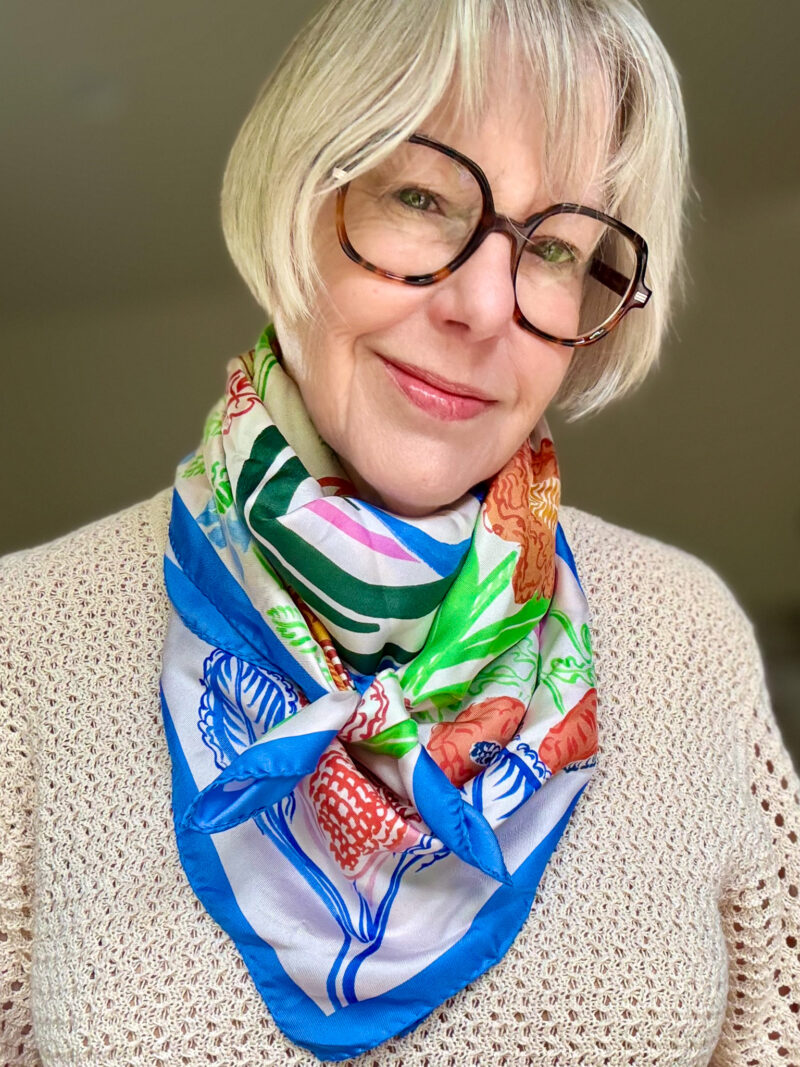 Susan B. wears a printed silk square scarf kerchief style, with the ends knotted in the front.