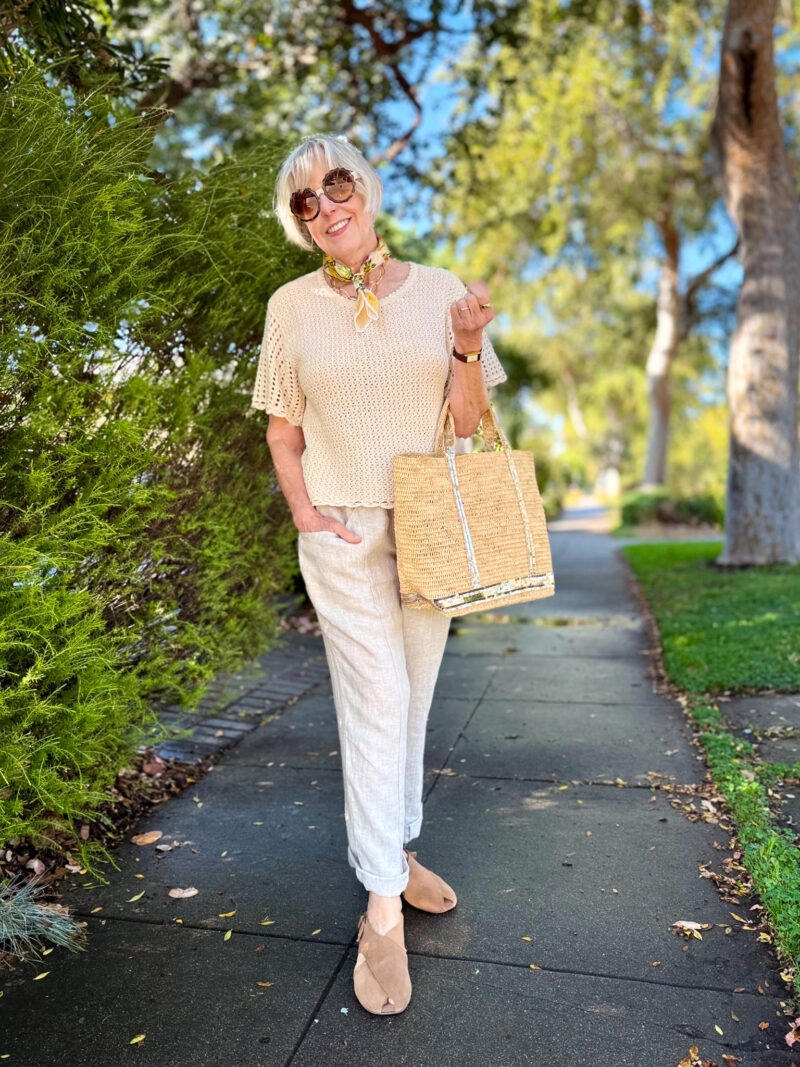 Monochrome summer outfit with a cream crochet top, natural linen pants, suede slingback flats, and a Vanessa Bruno Cabas raffia tote with sequin stripes