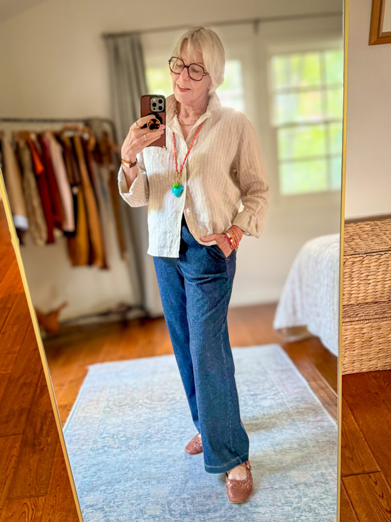 Beige striped linen button-down shirt worn open over a white top, with dark wash straight-leg drawstring jeans and brown open weave mary jane flats