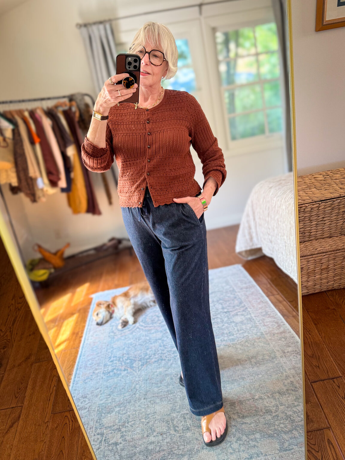 Rust crochet cardigan with dark wash straight-leg drawstring denim pants and tan sandals.