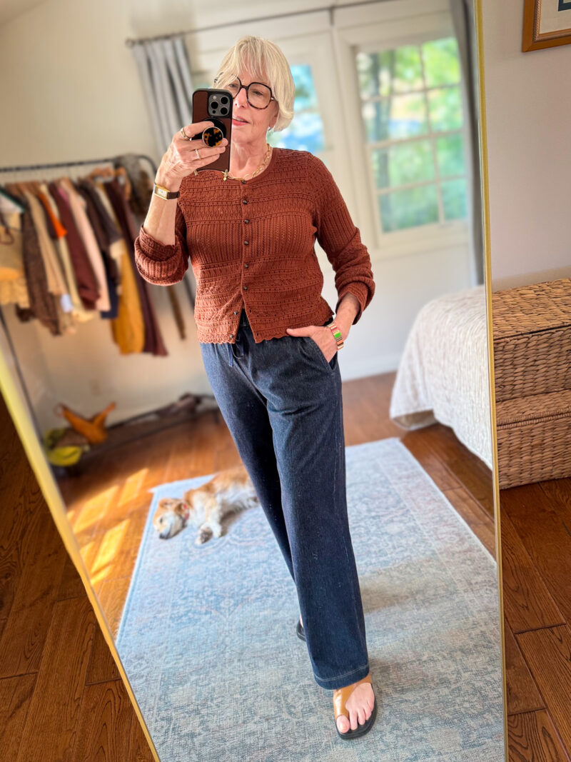 Rust crochet cardigan with dark wash straight-leg drawstring denim pants and tan sandals.