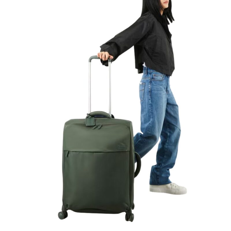 Woman wearing a black top and jeans rolls an olive green Lipault spinner suitcase.