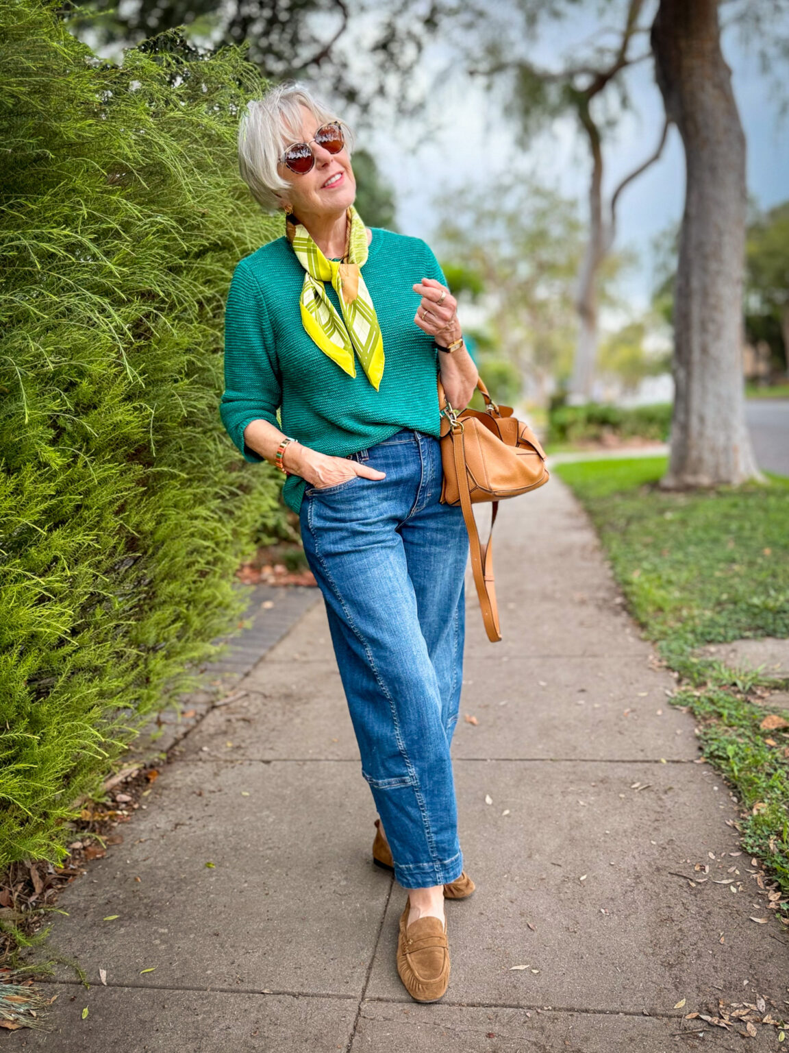 Casual jeans and teal sweater outfit styled for fall with a silk scarf, cognac handbag, sunglasses, and brown loafers.
