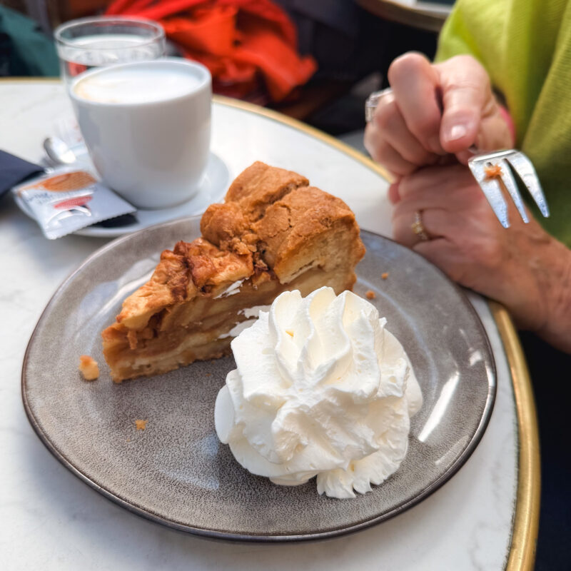 Traditional Netherlands apple cake with whipped cream. Woman holds fork ready to eat.