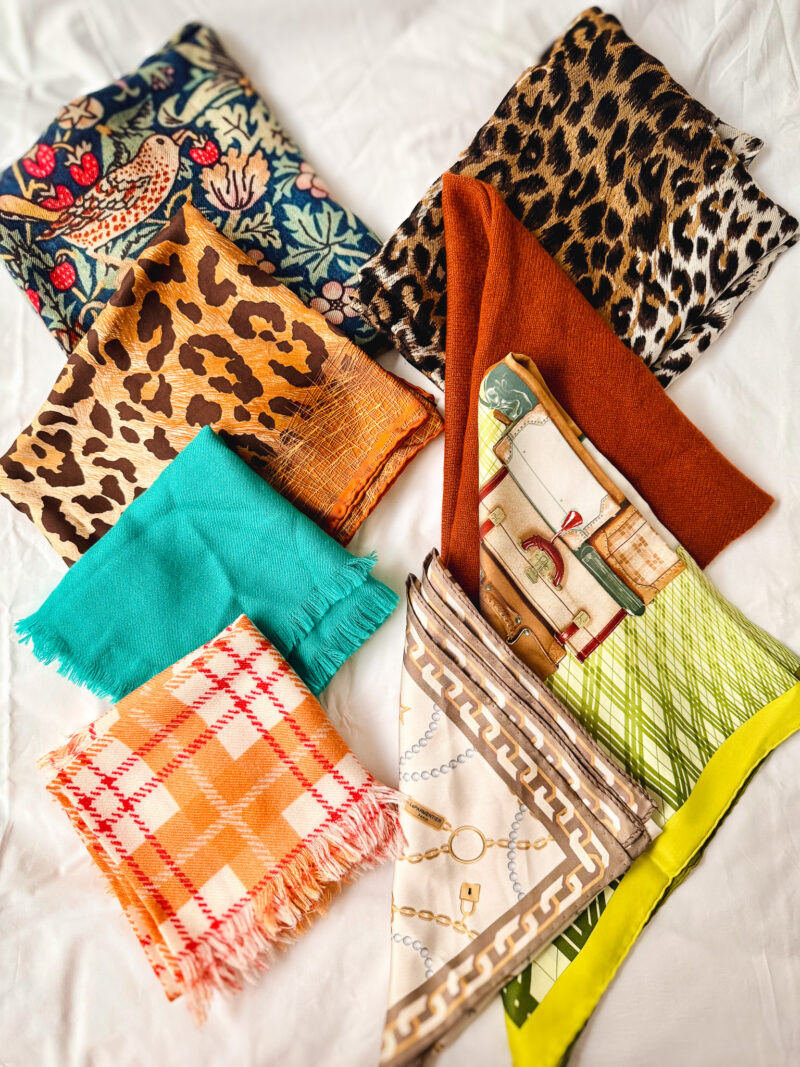 Scarves I packed for fall travel: silk cashmere Liberty print scarf, silk-cashmere leopard print scarf, leopard print silk carré, rust knit wool triangle scarf, fringed cashmere square in aqua marine, fringed cashmere square in orange plaid, Hermes "H en Voyage" silk square, beige silk bandana.