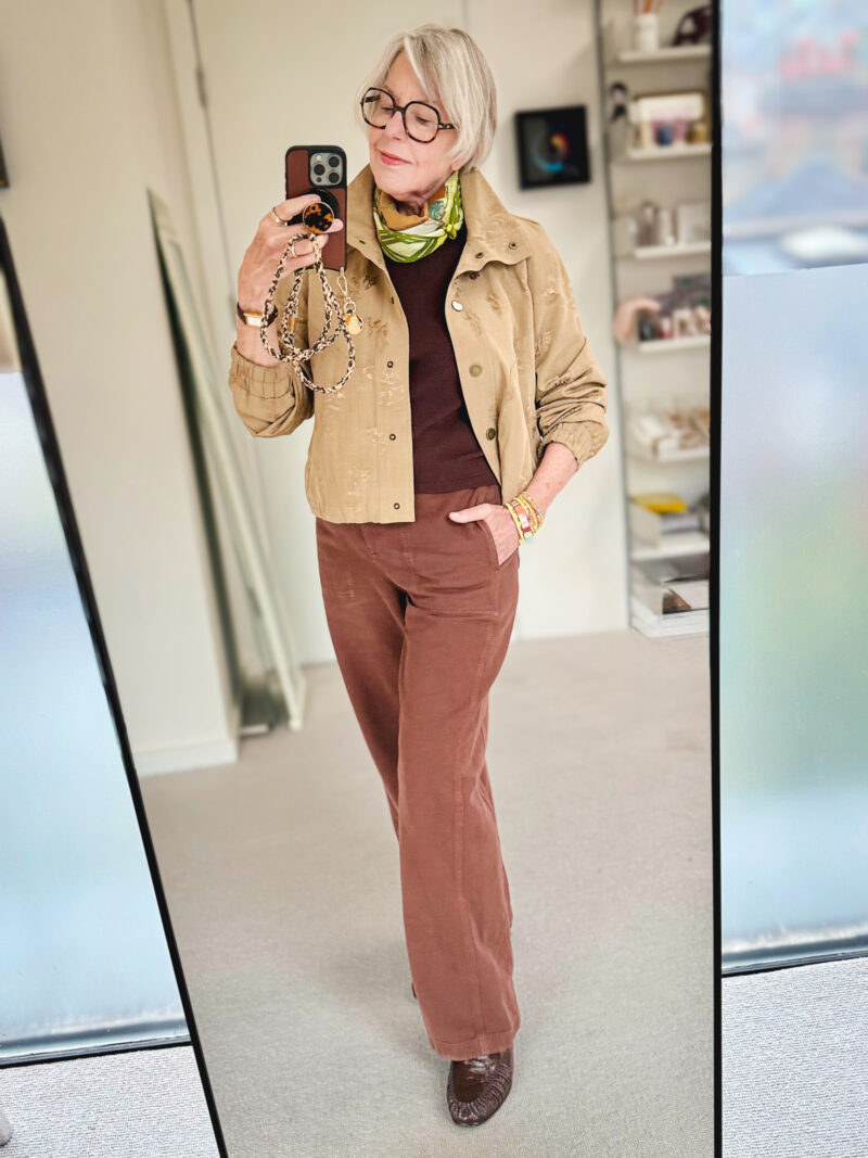 Mirror selfie of a woman wearing a tan floral jacket over a dark brown top, rust trousers, a green patterned scarf and brown loafers.