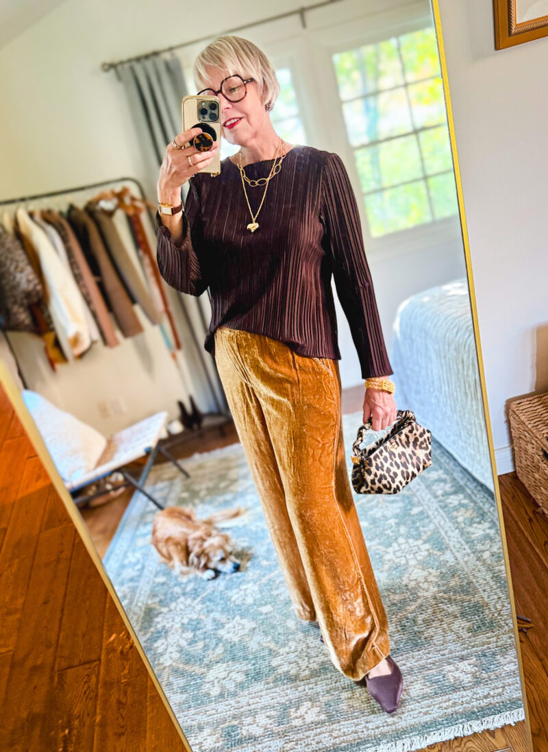 Susan styles gold velvet pants with a dark pleated top, pointed shoes, and a leopard-print handbag.